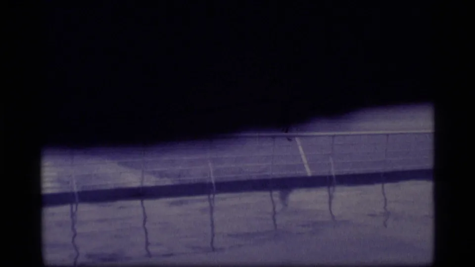 Partly obscured 8mm frame of the ship deck, showing railings, wet reflections, open water, and the American flag near the right side.
