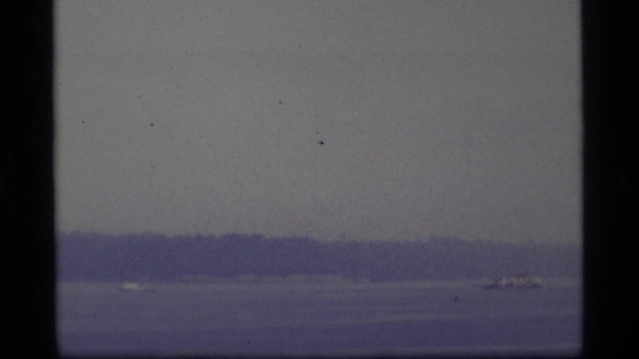 Distant boat on calm water with hazy shoreline and pale sky.