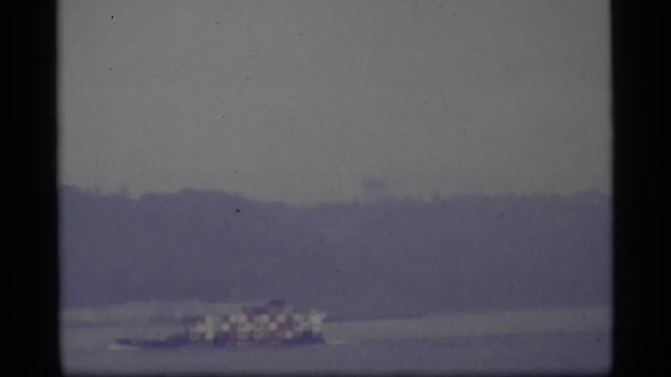 1977 Alaska 8mm still of a small boat with a red-and-white-looking canopy crossing calm water.