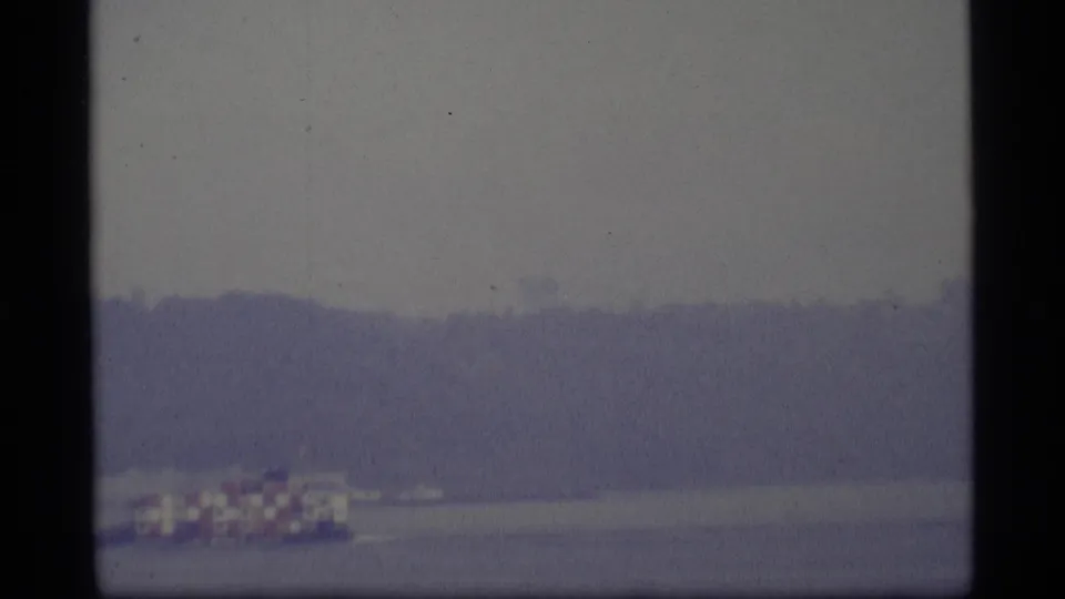 1977 Alaska home-movie frame showing the small canopy boat continuing across calm water near the lower edge.