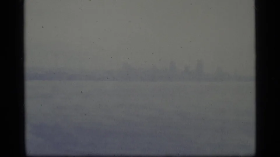 Distant Seattle-area skyline appears faintly through fog over gray harbor water in a soft 8mm frame.