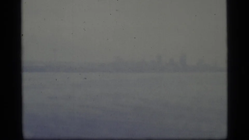 A subdued 8mm harbor view shows gray water and a barely defined shoreline under dense haze.