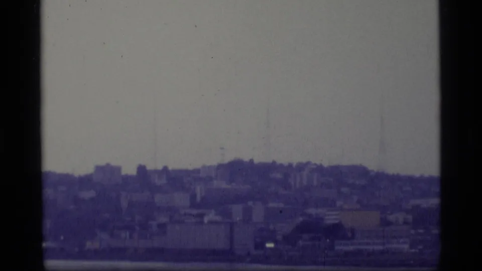 Hazy 1977 Alaska waterfront view with distant buildings, hills, and visible 8mm gate edges.