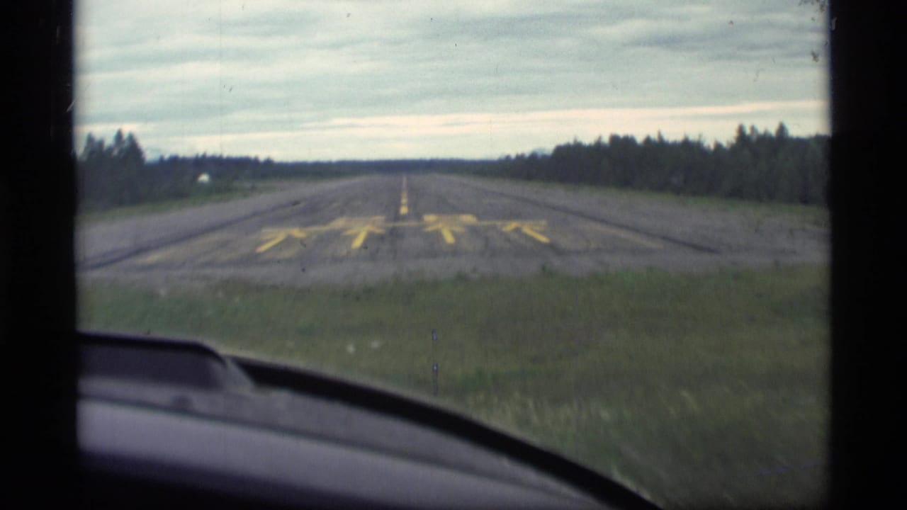 Runway 28 seen through a vehicle windshield with forest along both sides.
