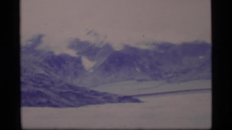 1977 Alaska 8mm frame showing a wide snow-covered mountain landscape with ridgelines, soft focus, and faded purple-blue color.
