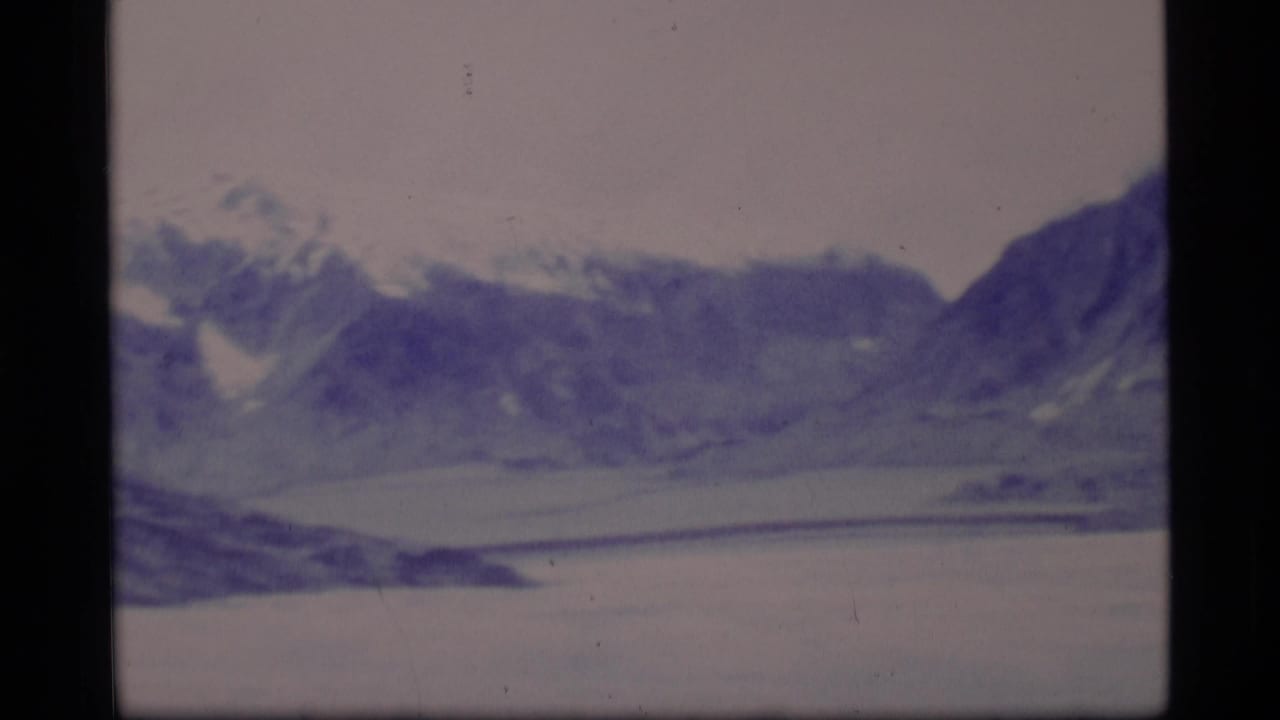 Soft-focus mountain range beyond a pale frozen lake under an overcast sky.