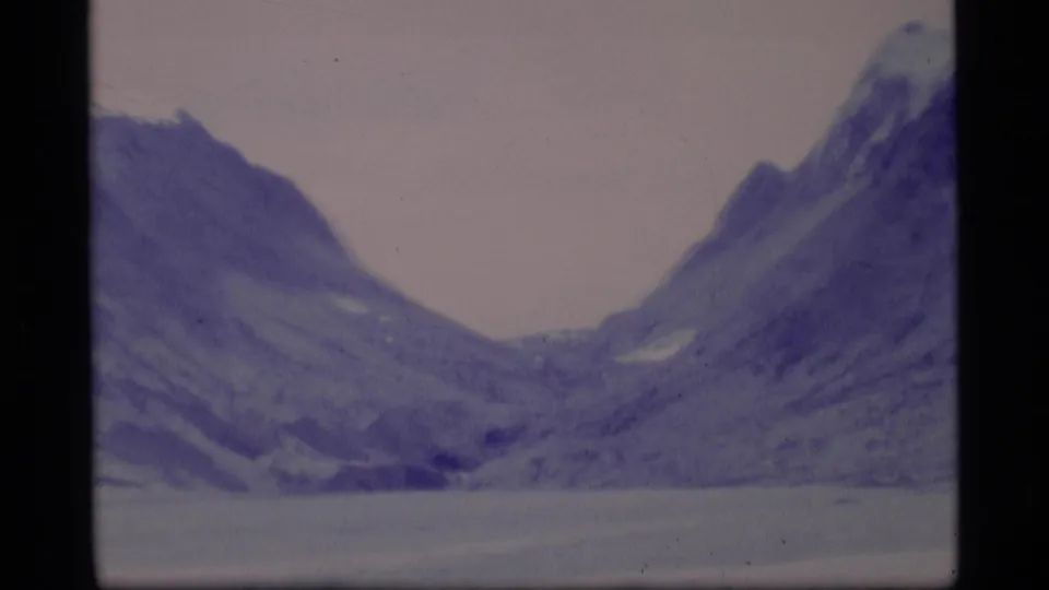 1977 Alaska 8mm frame of a wide mountain pass or valley, with steep snow-streaked slopes and soft home-movie color.