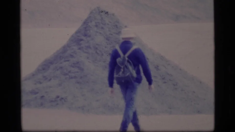 The backpacked figure continues toward the conical snow or ice mound in the 1977 Alaska winter travel footage.