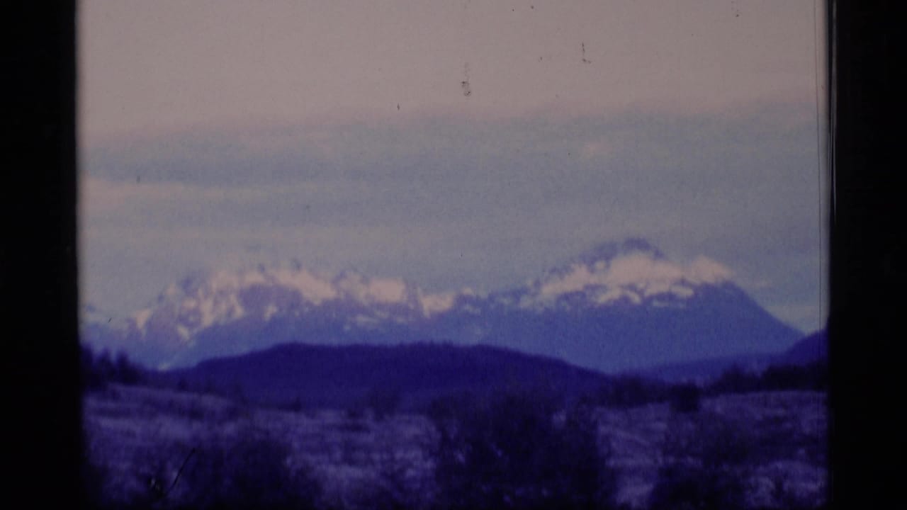 Distant snowy mountain range with dark foothills and film-frame borders.