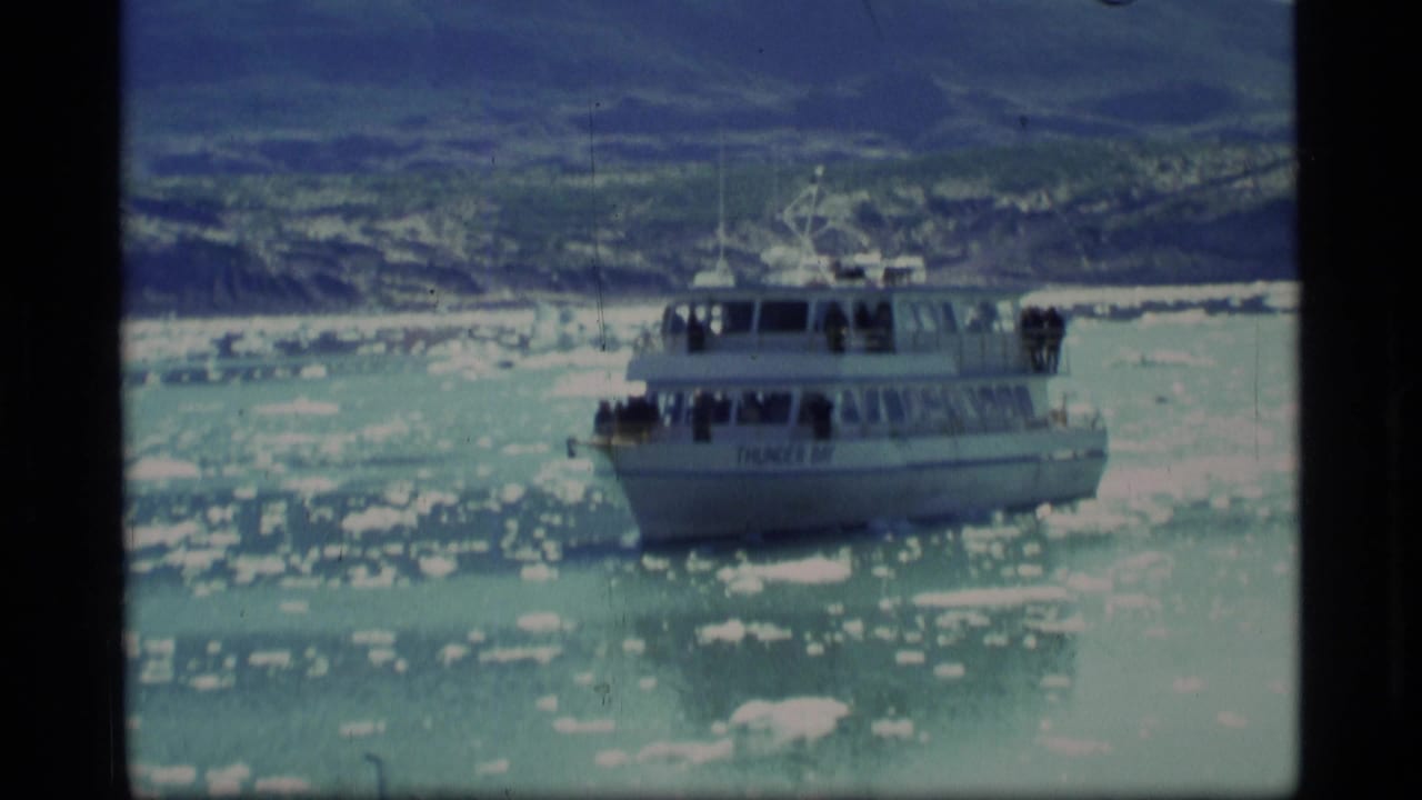 Tour boat moving through icy blue water with snowy mountains in the distance.