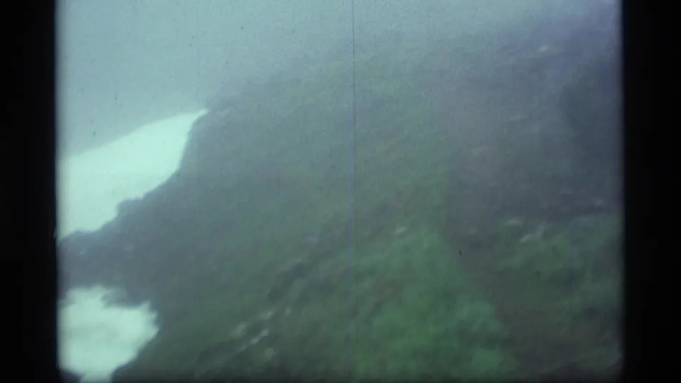 1977 Alaska 8mm view of a distant mountain valley with pale snow or water cutting through dark green terrain.