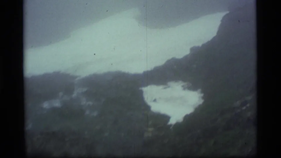 1977 Alaska 8mm frame looking across a high mountain ridge with pale snowfield or water in the valley below.