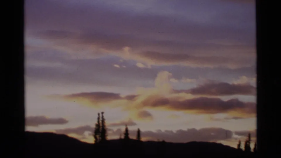 1977 Alaska 8mm view of sunset clouds fading over low hills and sparse silhouetted trees.