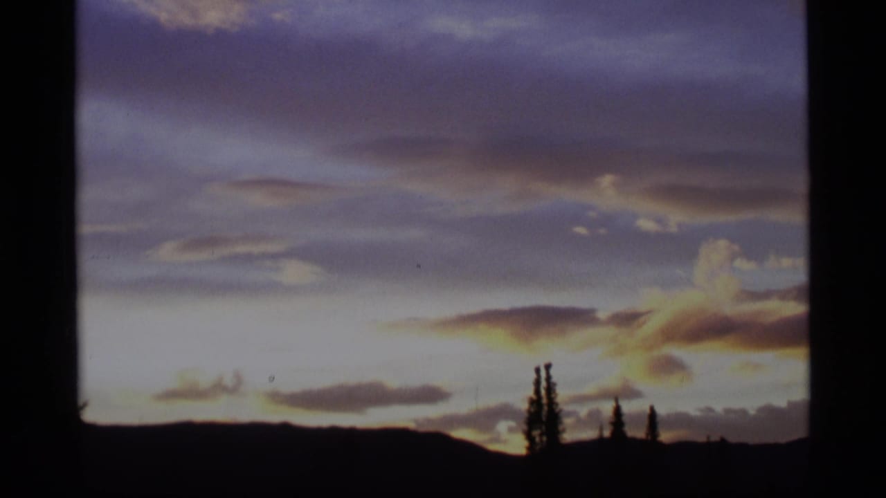 Sunset sky over dark hills and tree silhouettes within an 8mm film frame.
