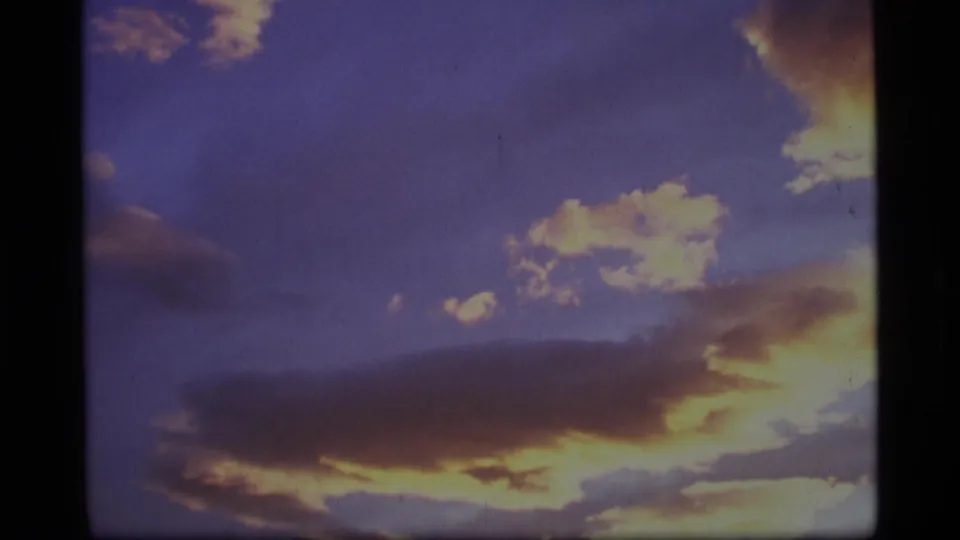 1977 Alaska home-movie frame with glowing cloud edges filling most of the evening sky.