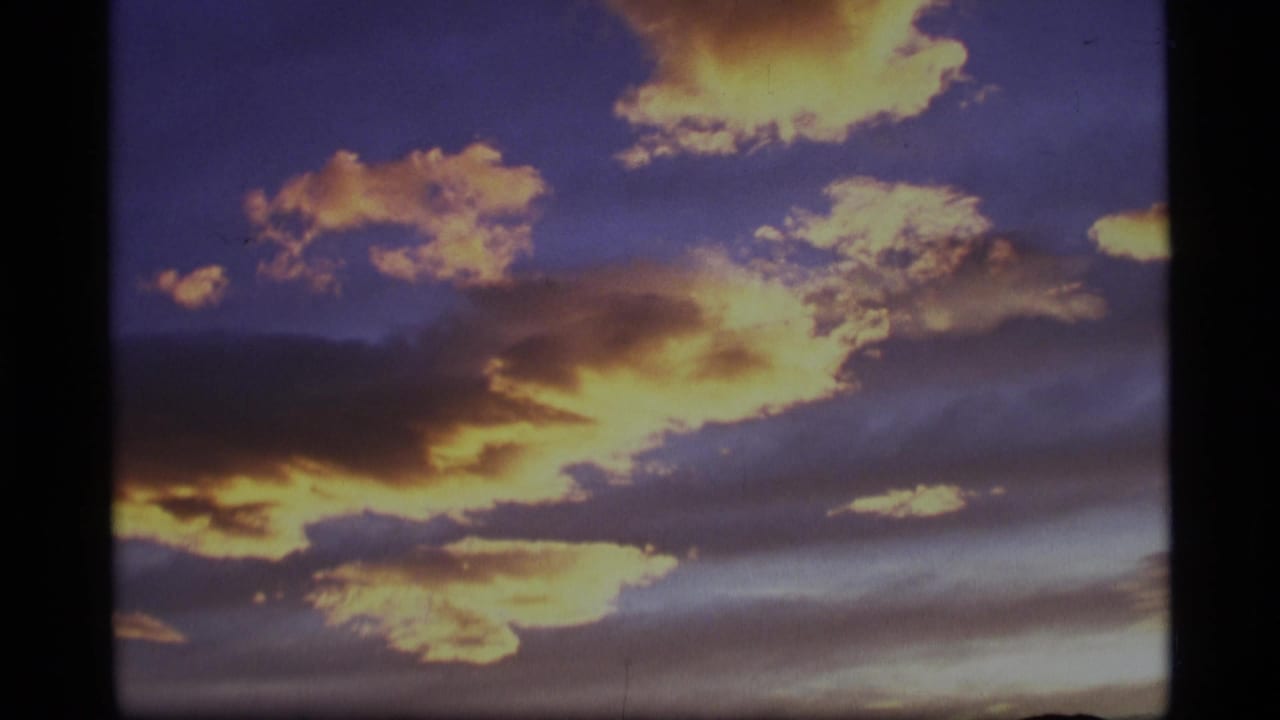 Yellow sunset clouds over a dark mountain horizon in a blue-gray sky.