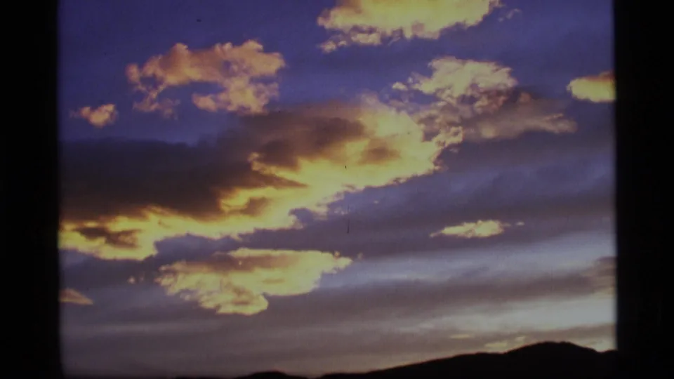 Vintage 8mm Alaska landscape frame with billowy yellow clouds and a low dark ridge at the bottom of the scene.
