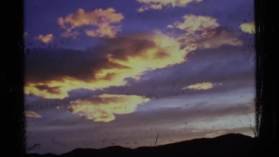 1977 Alaska 8mm frame with saturated sunset clouds, gray-blue sky, and dark rolling hills along the horizon.