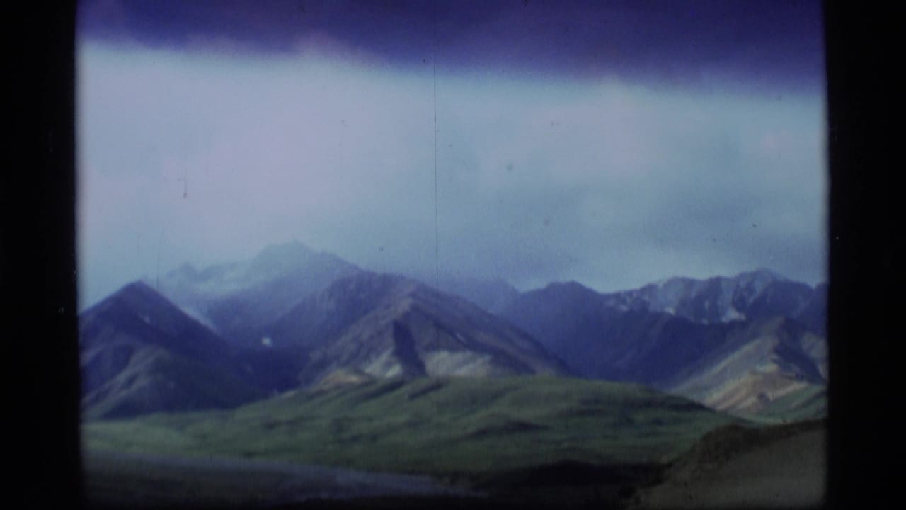 1977 Alaska 8mm frame showing rugged mountain ridges beneath a muted sky, with soft focus and aged-film color shift.