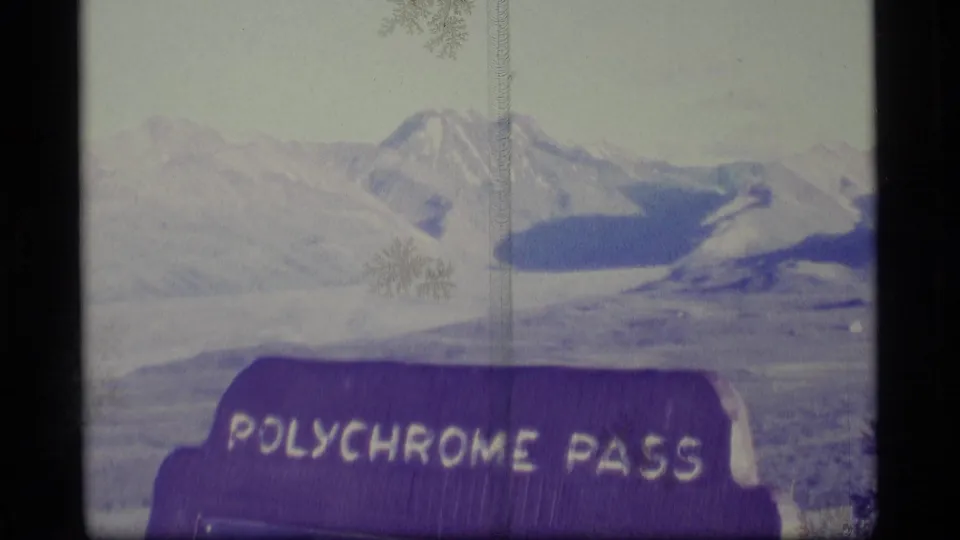 1977 Alaska 8mm frame showing snow-dusted mountains and a readable Polychrome Pass sign in the foreground.