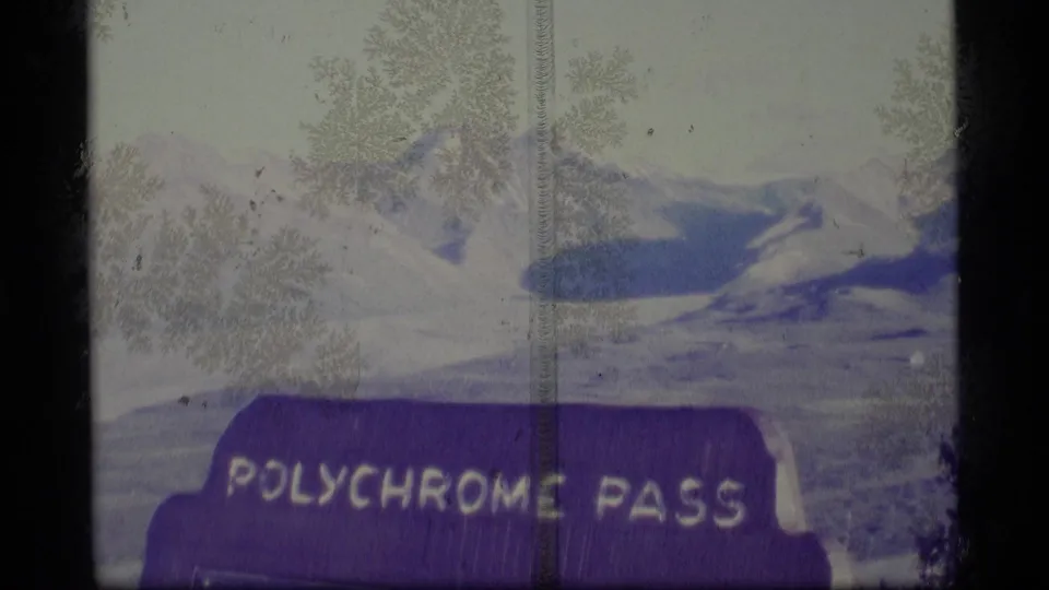 Faded 1977 Alaska 8mm view of the Polychrome Pass sign set against snow-dusted mountain peaks.