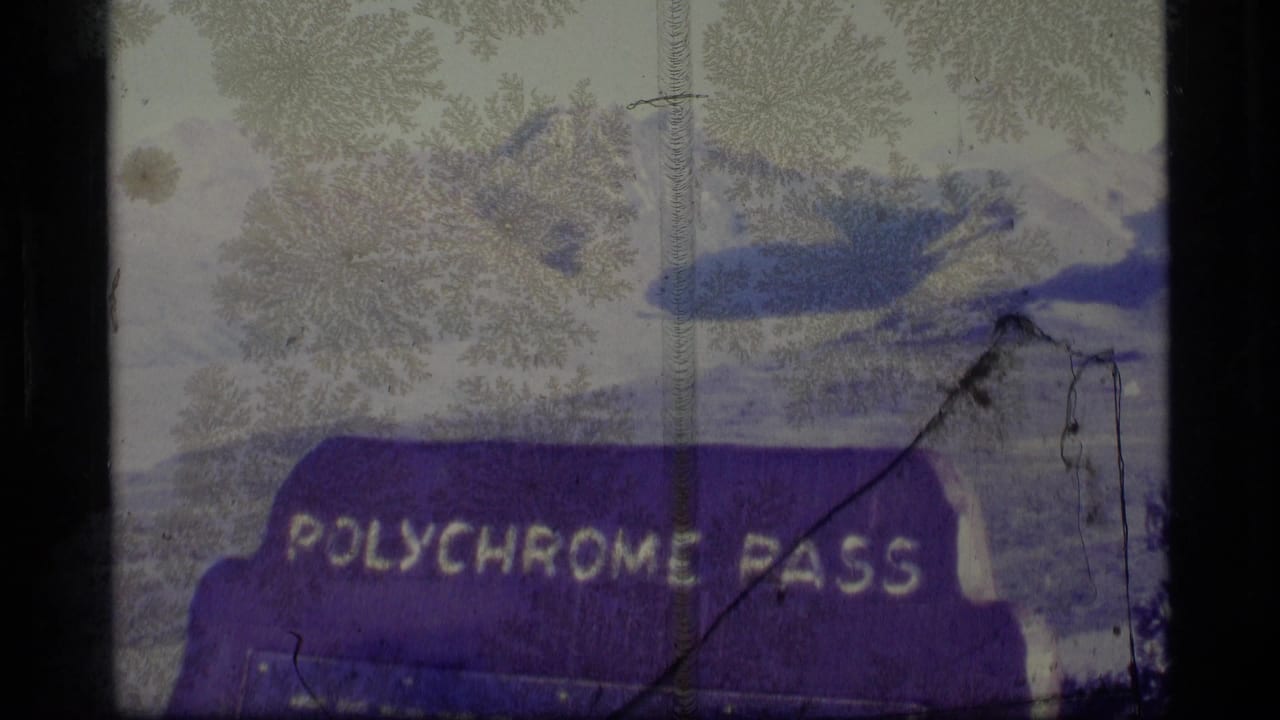 1977 Alaska 8mm frame showing a purple Polychrome Pass sign with pale mountains and snow patches behind it.