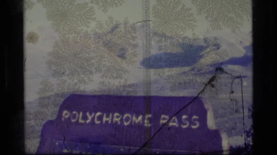 1977 Alaska 8mm frame showing a purple Polychrome Pass sign with pale mountains and snow patches behind it.