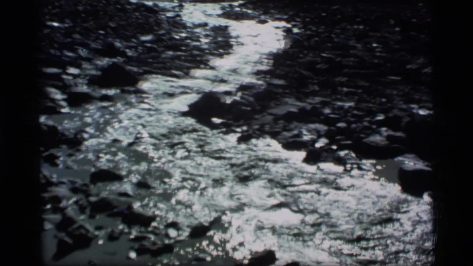 1977 Alaska 8mm frame showing bright reflected sunlight on fast-moving water in a rocky river channel.