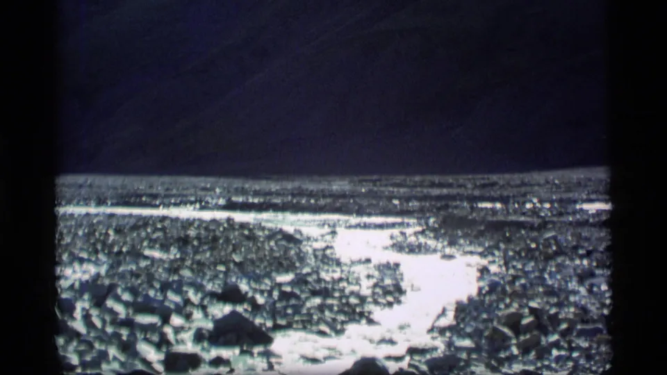 1977 Alaska 8mm frame showing a shallow rocky stream with strong water glare and dark exposure above.