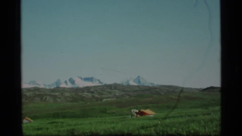 1977 Alaska 8mm view of a wide green campsite field with small tents and distant snowy peaks.