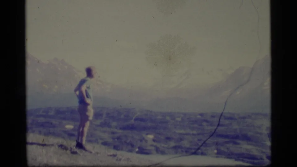 A late-1970s Alaska home-movie view shows the man in profile or from behind, watching the valley below.