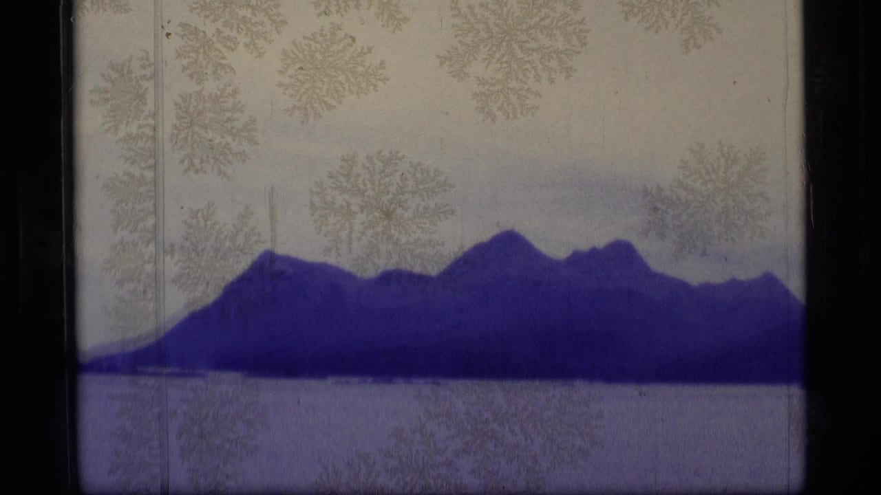 Snow-dusted mountain ridge across calm water, seen through aged 8mm film edges.
