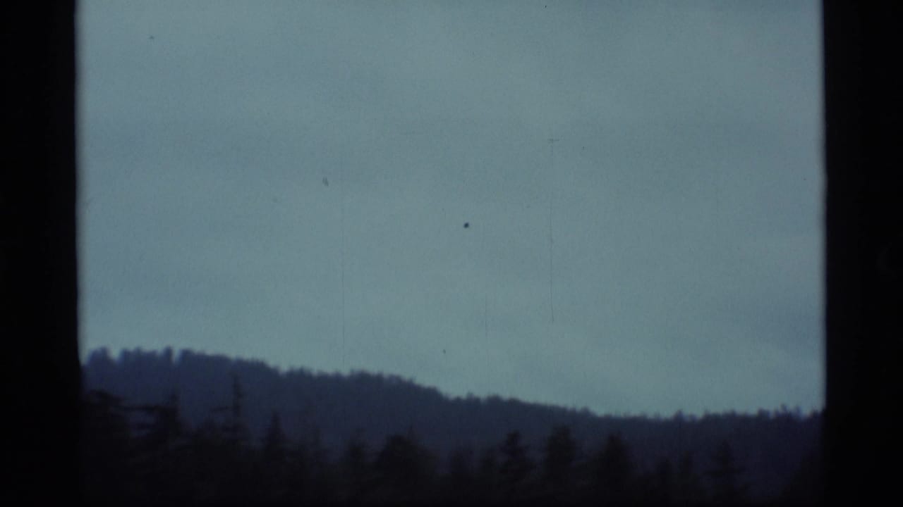 Cloudy sky over a dark forested ridge, framed by black vertical bars.
