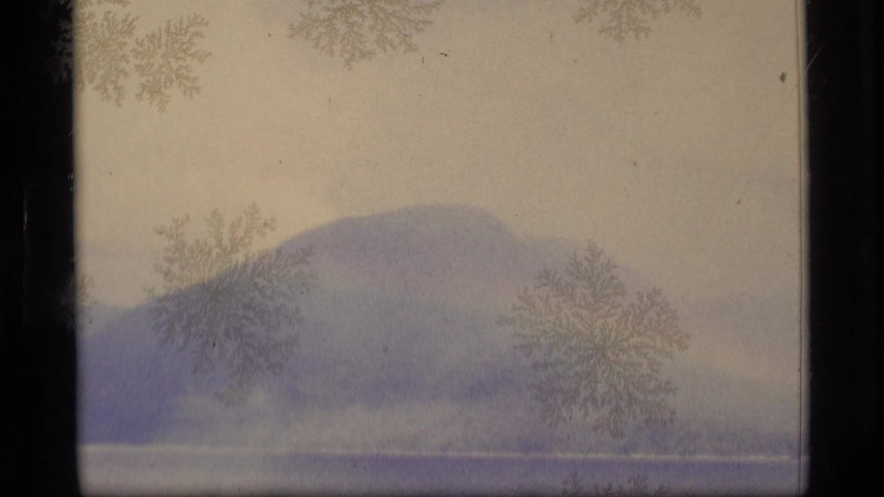 1977 Alaska 8mm frame with a hazy mountain ridge, pale waterline, frost-like marks, and dark film borders.