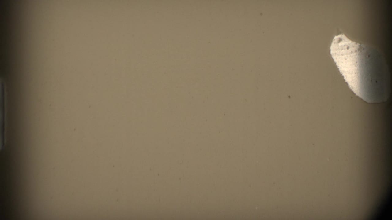 Mostly tan film frame with dark borders and a pale torn-looking mark near the upper right.