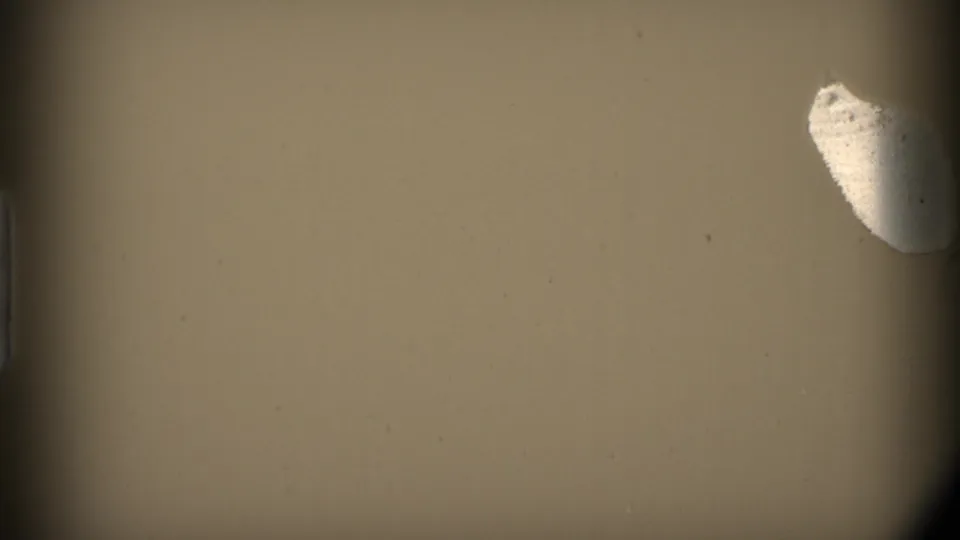 A mostly obscured 8mm frame showing tan exposure, dark film edges, and a pale irregular mark near the upper right.