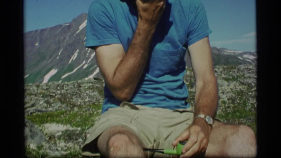 The 1977 Alaska frame shows a man seated outdoors, cropped at the face, with a pipe in hand and alpine peaks behind him.
