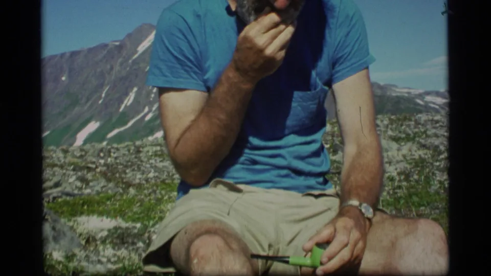 The final 1977 Alaska frame shows the man rubbing his beard while seated in shorts on a rocky alpine slope with distant peaks.