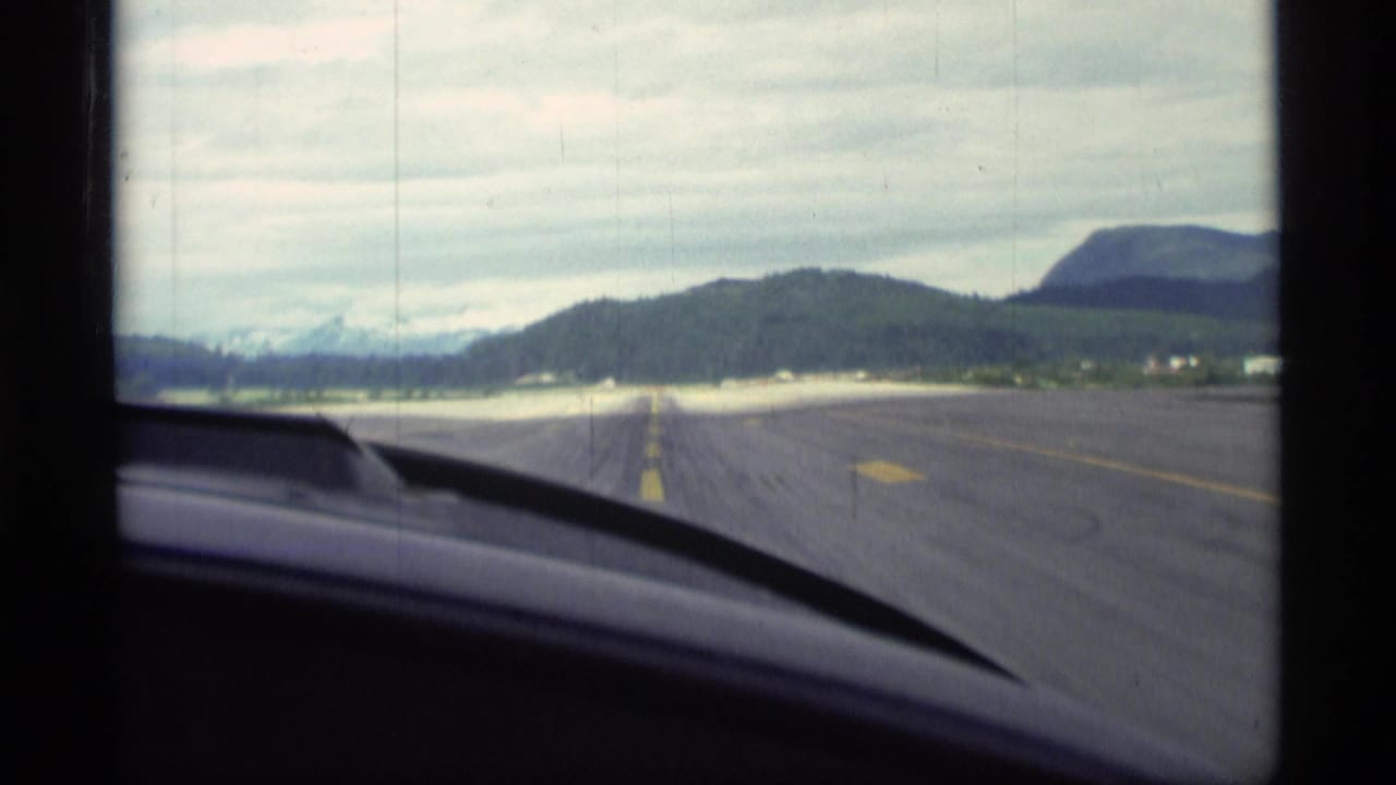 View through a vehicle windshield along a paved road toward low hills and distant mountains.