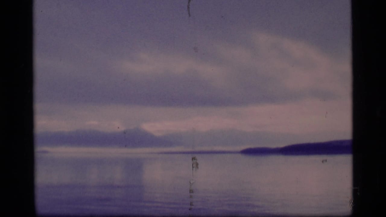 Wide water view with distant mountain silhouettes and shoreline at right beneath clouds.
