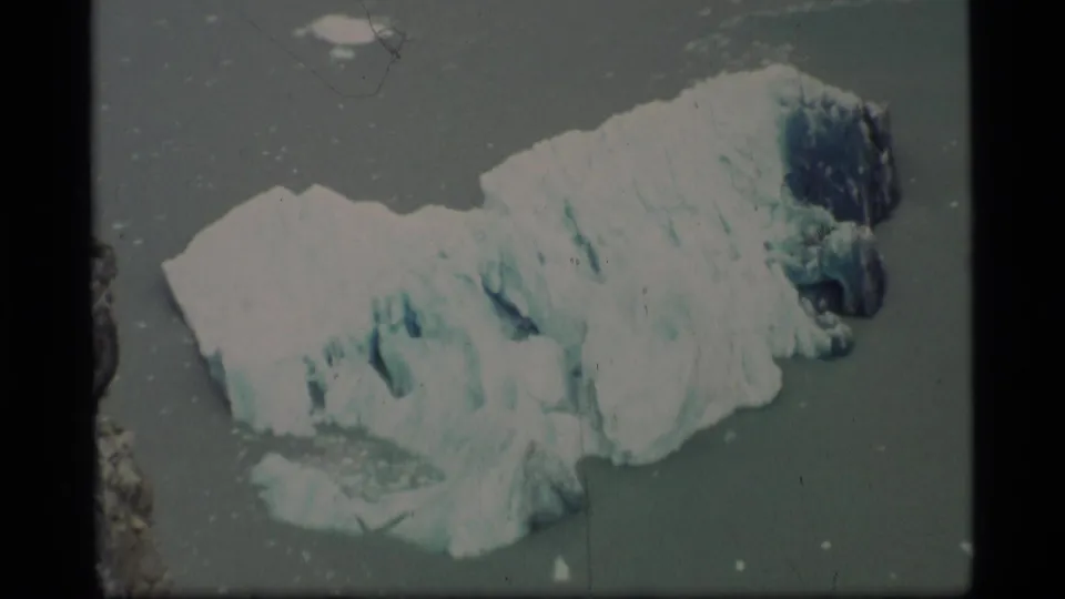 1977 Alaska 8mm frame showing the glacier chunk close in frame, with textured white ice and blue-shadowed crevasses.