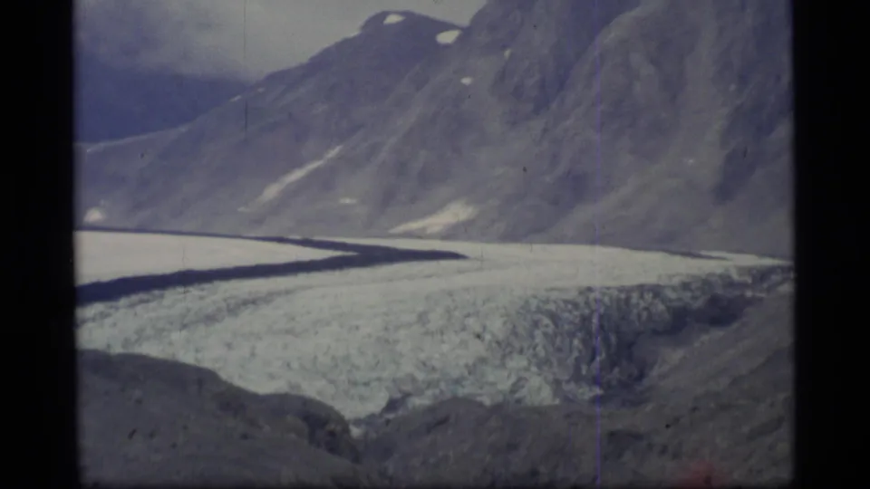 1977 Alaska 8mm view looking across glacier ice toward steep rocky slopes with small snow patches.