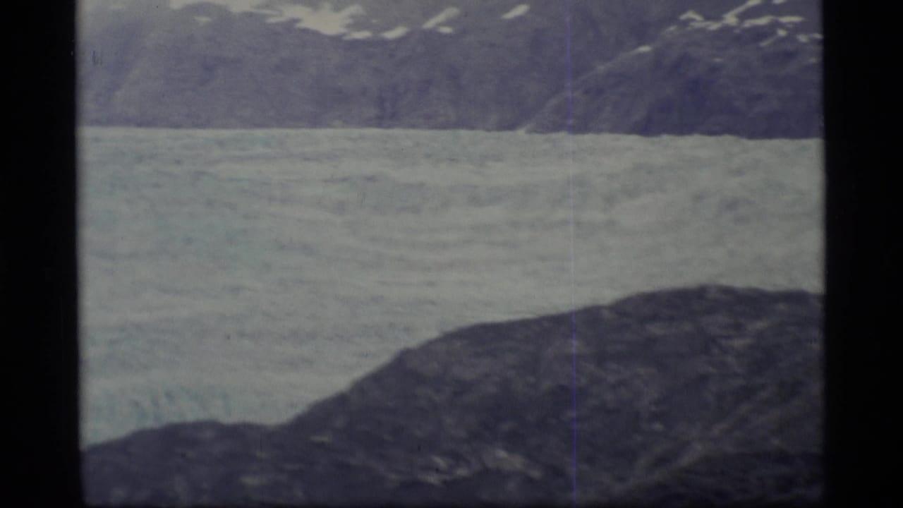 Glacier or frozen river below dark rocky mountains.