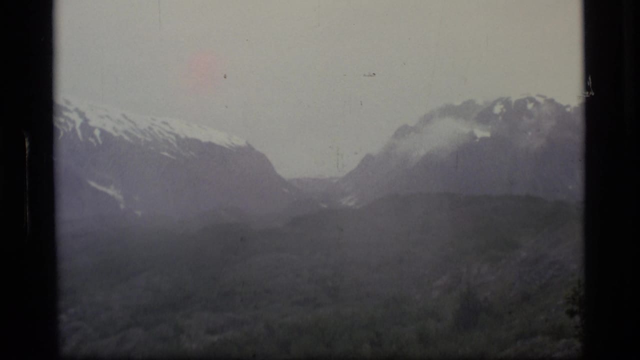 Snowy mountain range with cloud drifting around the peaks and a dark foreground ridge.
