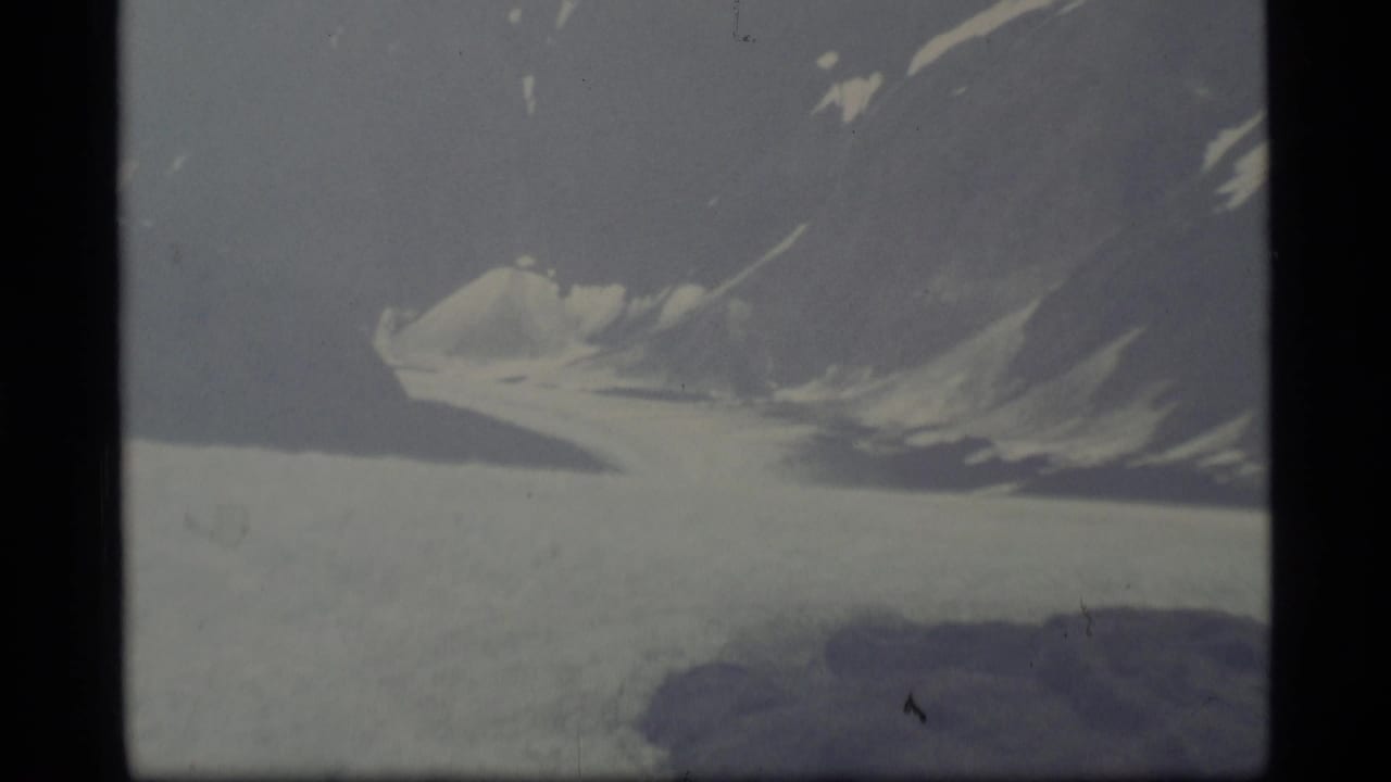 Snow-covered glacier and mountain ridge under hazy sky.
