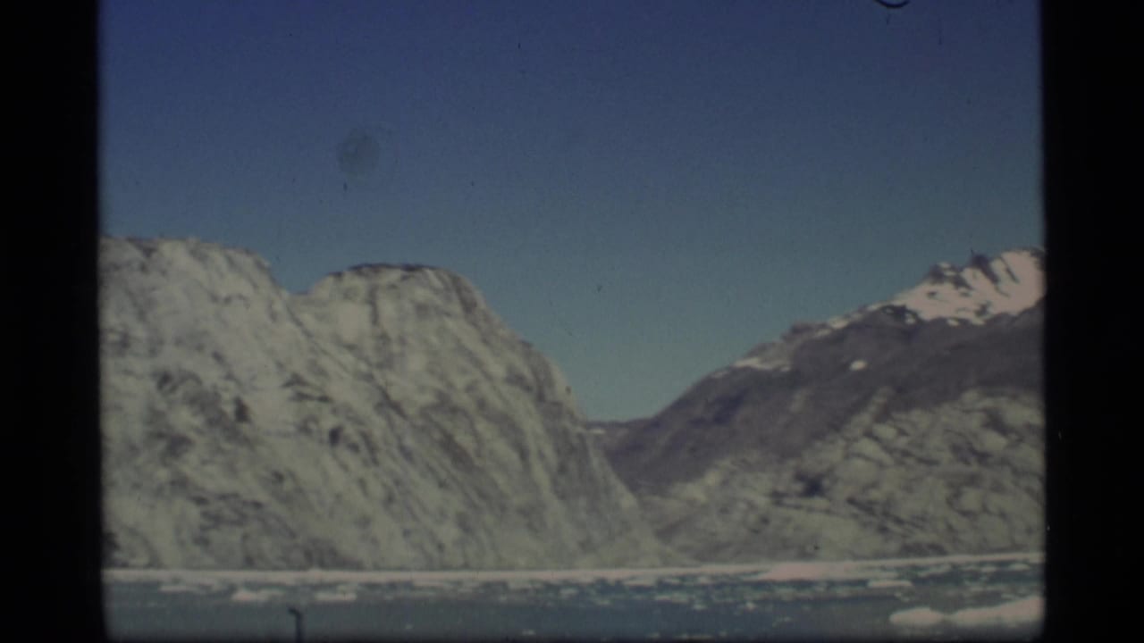Snow-streaked rocky mountains above icy water under a clear blue sky.