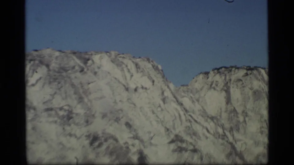 1977 Alaska 8mm frame focused on rugged snow-marked mountain ridges, with a clear blue sky and soft film texture.