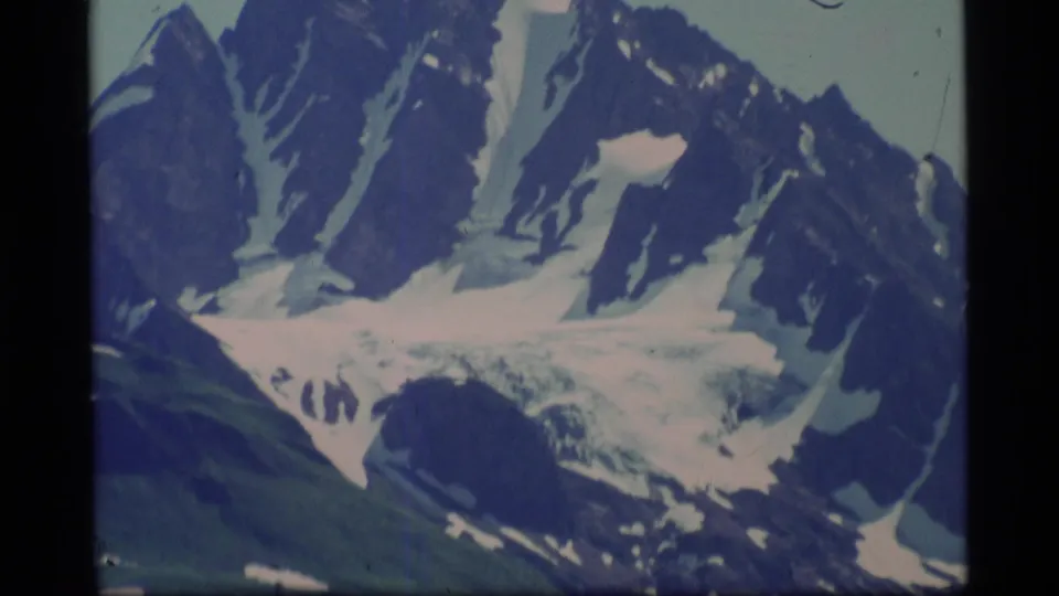 1977 Alaska 8mm frame holding on a snow-lined mountain ridge with glacier ice across the lower slope.
