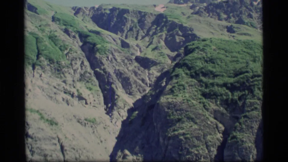 1977 Alaska 8mm view across green alpine slopes and rocky terrain toward distant ice and snow.