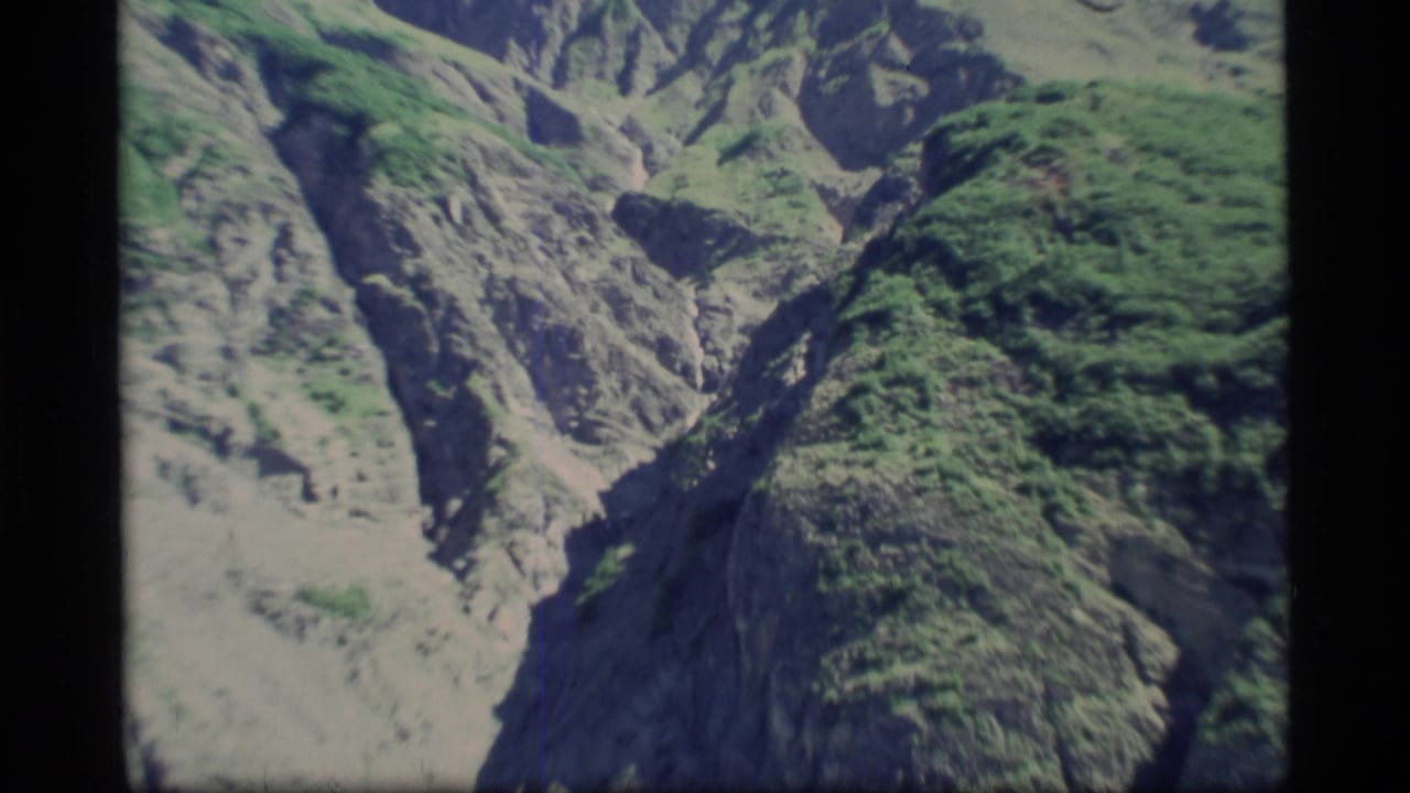Rocky green mountain slopes seen through black 8mm film borders.